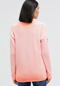 Pink ombre knit sweater featuring ribbed texture, loose fit, and wide sleeves. Subtle horizontal stripes are present throughout the design.