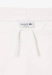 Bílé tapered jogger kalhoty s šňůrkou, s texturovaným pasem a s označením Lacoste s logem zeleného krokodýla.