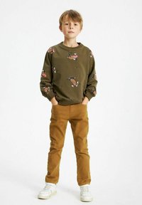 Olivgrön sweatshirt med mönstrade tecknade karaktärer, tillsammans med tanfärgade byxor. Outfiten har en avslappnad passform och långa ärmar.