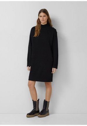 Zwart gebreid jurk met een hoge kraag, ribbelboorden en zoom. Gecombineerd met zwarte enkellaarsjes met een gestructureerd elastisch paneel.