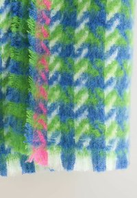 Fuzzy strikket stof med blå, grøn, hvid og pink houndstooth mønster og en lodret pink stribe på venstre side.