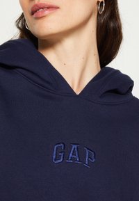 Sudadera con capucha en navy que presenta el logo "GAP" bordado. Fabricada en un tejido suave con un corte clásico y una textura sutil.