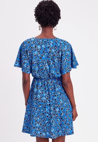 Bloemenpatroon blauwe jurk met korte vlindermouwen, geplooid middel en knoopdetail op de rug; heeft een klein zwart-wit bloemenpatroon.