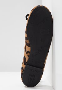 Chaussure à imprimé léopard avec une texture douce et velue. Semelle en caoutchouc noir avec un design de ballerine en relief et le nom de la marque.