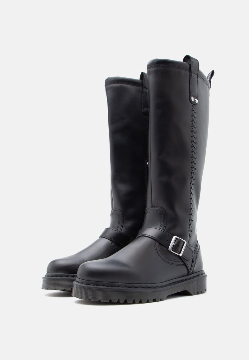 Ein Paar hohe schwarze Lederstiefel mit geschnallten Riemen und genähten Details, ausgestattet mit dicken profilierten Sohlen auf einem weißen Hintergrund.