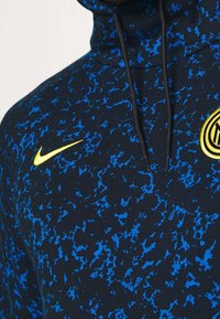 Sweat à capuche noir avec un motif abstrait bleu, comportant un logo Nike jaune et un emblème de l'Inter Milan. Il possède un col montant et des cordons de serrage.