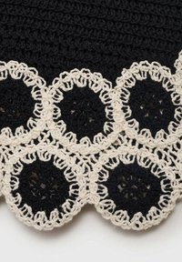 Schwarzer Häkelstoff mit weißen, kreisförmigen Spitzenakzenten, einer gewellten Kante und filigranen Mustern aus Kreisen und Blumen.