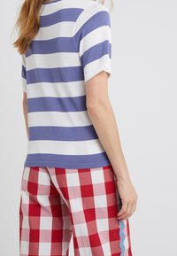 Mujer vistiendo una camisa de manga corta con rayas horizontales en azul y blanco, y pantalones a cuadros rojos y blancos con un ribete azul en forma de ola.