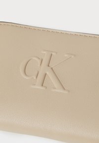 Portafoglio in pelle beige con logo "CK" impresso, texture liscia e cuciture precise lungo i bordi.