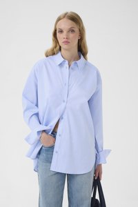 Camisa azul claro abotonada hecha de algodón, con un ajuste relajado, cuello clásico y mangas largas. Combinada con jeans de mezclilla clara.