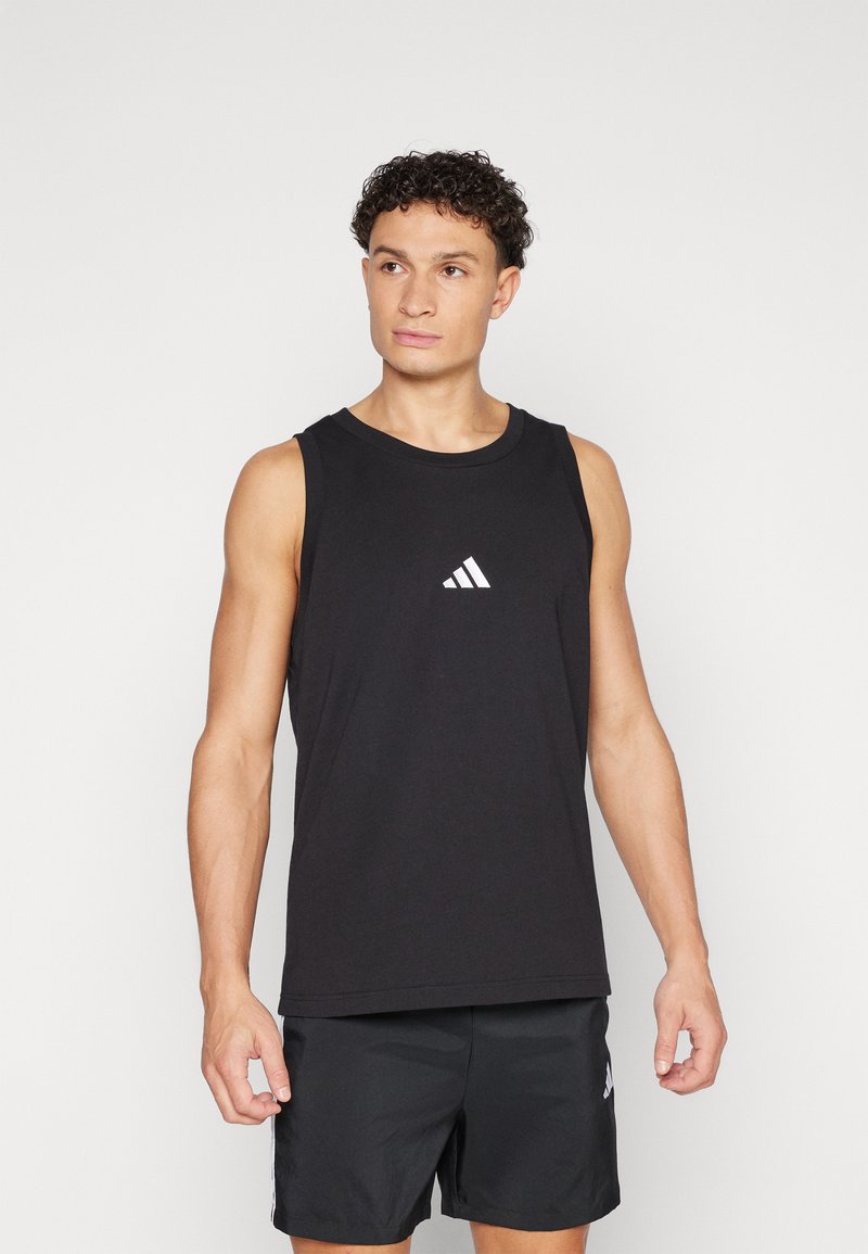 Camisola desportiva preta sem mangas feita de uma mistura de algodão, com um pequeno logótipo branco da Adidas no peito, acompanhada de calções escuros.
