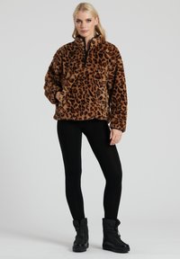 Brun leopardmønstret pullover lavet af blødt stof med en lynlåsekrave, to forlommer og en afslappet pasform. Bæres med sorte leggings.