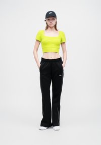 Pulover scurt de culoare verde deschis, cu mâneci scurte și tricotat texturat. Pantaloni negri, largi, cu dungi albe pe lateral. Căciulă neagră cu logo.