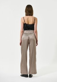 Camicetta in satin nero abbinata a pantaloni larghi a righe nei toni del beige e marrone. Vestibilità rilassata con vita elasticizzata e stampa geometrica.