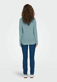 Maglione azzurro chiaro di tessuto lavorato, con maniche lunghe, scollatura tonda e orlo curvo, abbinato a jeans in denim scuro e sneakers bianche.