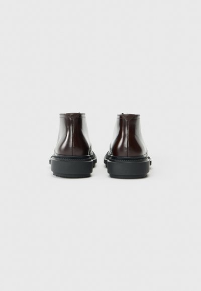 Hnedé lesklé kožené ankle topánky s plochou čiernou podrážkou, s elegantným dizajnom a minimalistickým prešitím na zadnej strane.