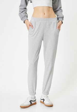 Grijze sweatpants van zachte stof, met een elastische tailleband, zijzakken en taps toelopende boorden. Gedragen met witte sneakers.