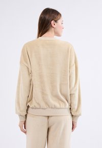 Beżowy polarowy sweter z luźnym krojem, prążkowanymi mankietami i elastycznym dołem. Miękka faktura z minimalną ilością szwów, wykończony okrągłym dekoltem.