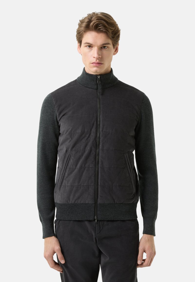 Sort og grå lynlåstrøje med en tekstureret krop, ribbet krave og manchetter samt sidelommer. Har en oppustet vatteret frontpanel.