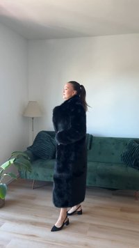 Melnā mākslīgā kažokā ar augstu apkakli, garām piedurknēm un taisnu griezumu. Iekrāsota ar spīdīgu tekstūru un apvienota ar melniem slingback zābakiem.