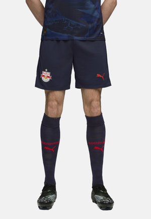 Marineblå fodboldshorts med Red Bull Salzburg-logo, sammen med knælange marineblå sokker med rød "SOIZBURG" tekst og Puma-logo. Sorte fodboldsko med designelementer.