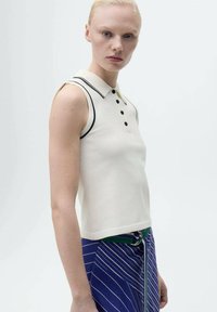 Top polo fără mâneci, de culoare crem, cu margini negre, nasturi pe față, asociat cu fustă în dungi albastre, accentuată cu o curea verde.