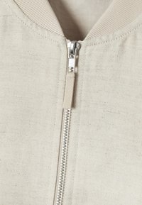 Lys beige zip-up jakke med tekstureret stof, ribbet halsudskæring og sølvfarvede lynlåsdetaljer. Standard pasform, minimalistisk design.