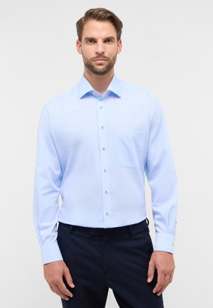 Hellblaues Langarmhemd mit spitzem Kragen, aufgesetzter Tasche und Knopfdetails. Der Stoff wirkt glatt und leicht strukturiert.