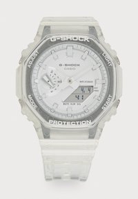 Transparent G-Shock watch with a round case, white dial, digital display, and silver accents. Features include a textured clear strap and water resistance.