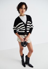 Black and white striped knitted cardigan with buttons, paired with light shorts and black knee-high boots. Accessories include a heart-shaped bag.