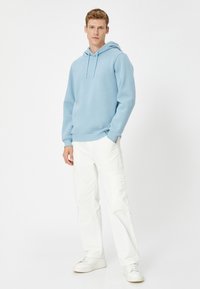 Sudadera azul claro con cordón, fabricada en tejido suave, de corte relajado, combinada con pantalones cargo blancos y zapatillas blancas. Diseño y esquema de colores simple.