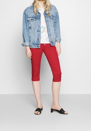 Giacca di jean, azzurro chiaro, con bottoni, due tasche sul petto; t-shirt bianca con stampa circolare; pantaloni rossi a vita alta; sandali neri con tacco.