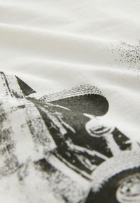 Schwarz-weißer, detaillierter Druck eines Vintage-Rennwagens auf strukturiertem weißem Stoff mit sichtbaren Reifenspuren und Umrissen des Wagenkörpers.