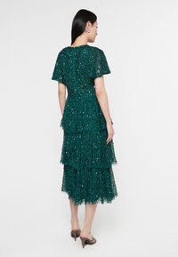 Teal välikiharat mekko lyhyillä hihoilla, koristeltu paljeteilla. Sisältää takakytkimen ja kerroksellisia frillejä, valmistettu teksturoidusta kankaasta.