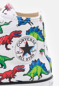 Bílé plátěné tenisky s barevnými pixelovanými vzory dinosaurů v červené, zelené a modré barvě, s černobílou nášivkou "Converse All Star".