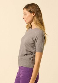 Pull gris à manches courtes en tissu doux, avec un col rond et des bords côtelés, porté avec un pantalon violet.