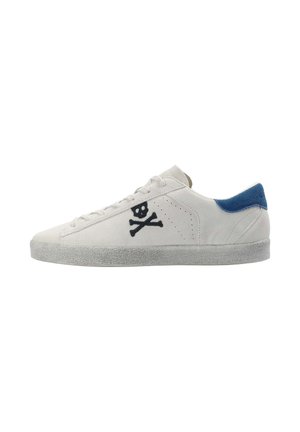 Zapatillas bajas de ante blanco con una pestaña en el talón azul. Cuentan con bordado de calavera y huesos cruzados en negro en el costado y suela texturizada en gris.