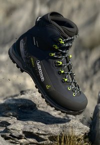 Černá turistická bota se šedými akcenty, texturovaným svrškem, jasně žlutými očky a tkaničkami; má robustní podrážku a technologii Gore-Tex.