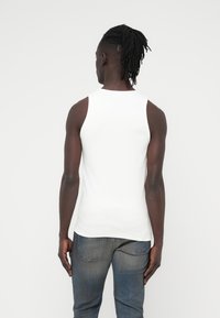 Λευκό αμάνικο τοπ από βαμβάκι, εφαρμοστό σχέδιο, λεία υφή, φορεμένο με σκούρο μπλε τζιν, φαίνεται από πίσω.