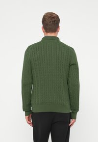 Pull en tricot vert avec un motif en torsade, col, poignets et ourlet côtelés. Coupe droite, tissu texturé et couleur unie.