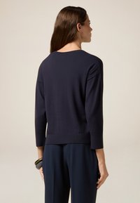 Maglione lavorato a maglia blu navy con maniche a tre quarti, scollo rotondo e fondo aderente. Texture liscia, dettagli minimi.