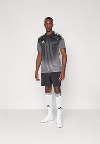 Maillot de sport gris avec des accents noirs et des détails vert fluo, shorts noirs, chaussettes blanches à rayures noires, et chaussures blanches.