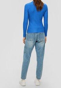 Maglietta blu a maniche lunghe con righe, abbinata a jeans chiari larghi con tasche laterali, indossata con sneakers bianche chunky.