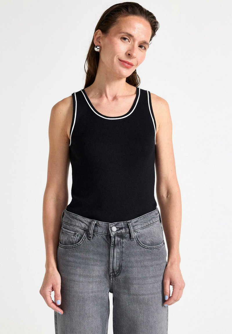Schwarzes geripptes Tanktop mit weißem Kontrastbesatz, kombiniert mit hellgrauen, hochgeschnittenen Jeans. Glatte Textur und figurbetonendes Design.