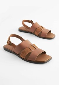 Hnědé kožené a semišové sandály s otevřenou špičkou, nastavitelním páskem a plochou podrážkou. Obsahují horizontální pásky a minimalistický styl.