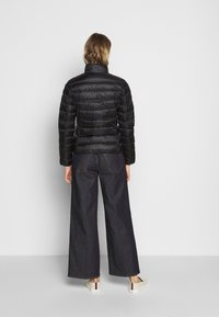 Sort pufferjakke med høj krave og quilted design, parret med brede mørk dunbukser og hvide sneakers.