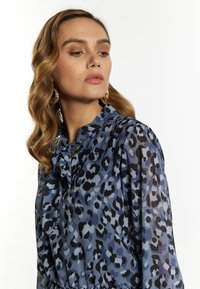 Luipaardprint blouse in blauwtinten en zwart, lichte stof, kraag met strikdetail, lange mouwen, gladde textuur.