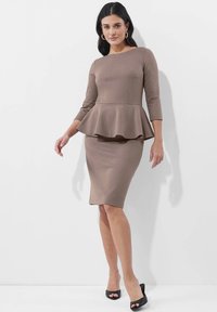Braunes Peplum-Kleid mit Dreiviertelärmeln, tailliertem Rock und glatter Textur. Verfügt über einen runden Halsausschnitt und einen modischen Saumabschluss, kombiniert mit schwarzen Absätzen.