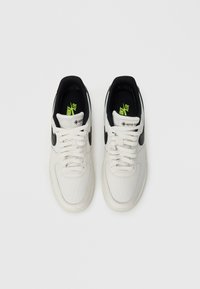 Par bijelih Nike Air tenisica s crnim swoosh logotipima, Gore-Tex oznakama na jezičcima i neon zelenim ulošcima, gledano odozgo na bijeloj pozadini.