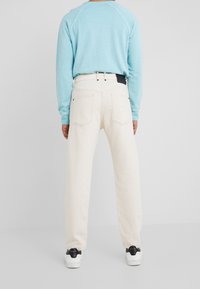 Pantalones de mezclilla de color claro con un corte relajado y costuras visibles. Combinados con un sudadera azul pastel y zapatillas blancas.
